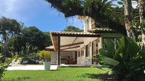 Una casa con porche techado, césped y plantas tropicales.