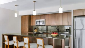 Cozinha moderna com ilha central, banquetas, eletrodomésticos de aço inoxidável e iluminação pendente.