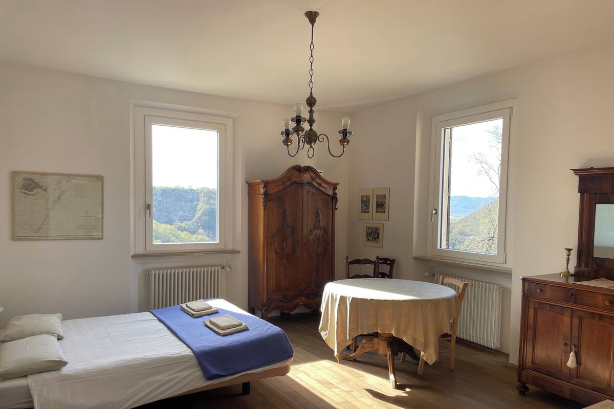 A bedroom with a bed, a table, a chair, a wooden cabinet, and a chandelier.