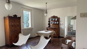 Un comedor con una mesa, sillas, un radiador, una ventana y un aparador de madera con platos.