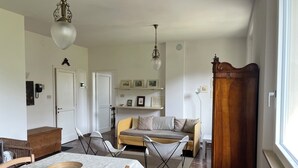 Una sala de estar con un sofá, sillas, una mesa de comedor con un tazón, un aparador de madera y una lámpara colgante.