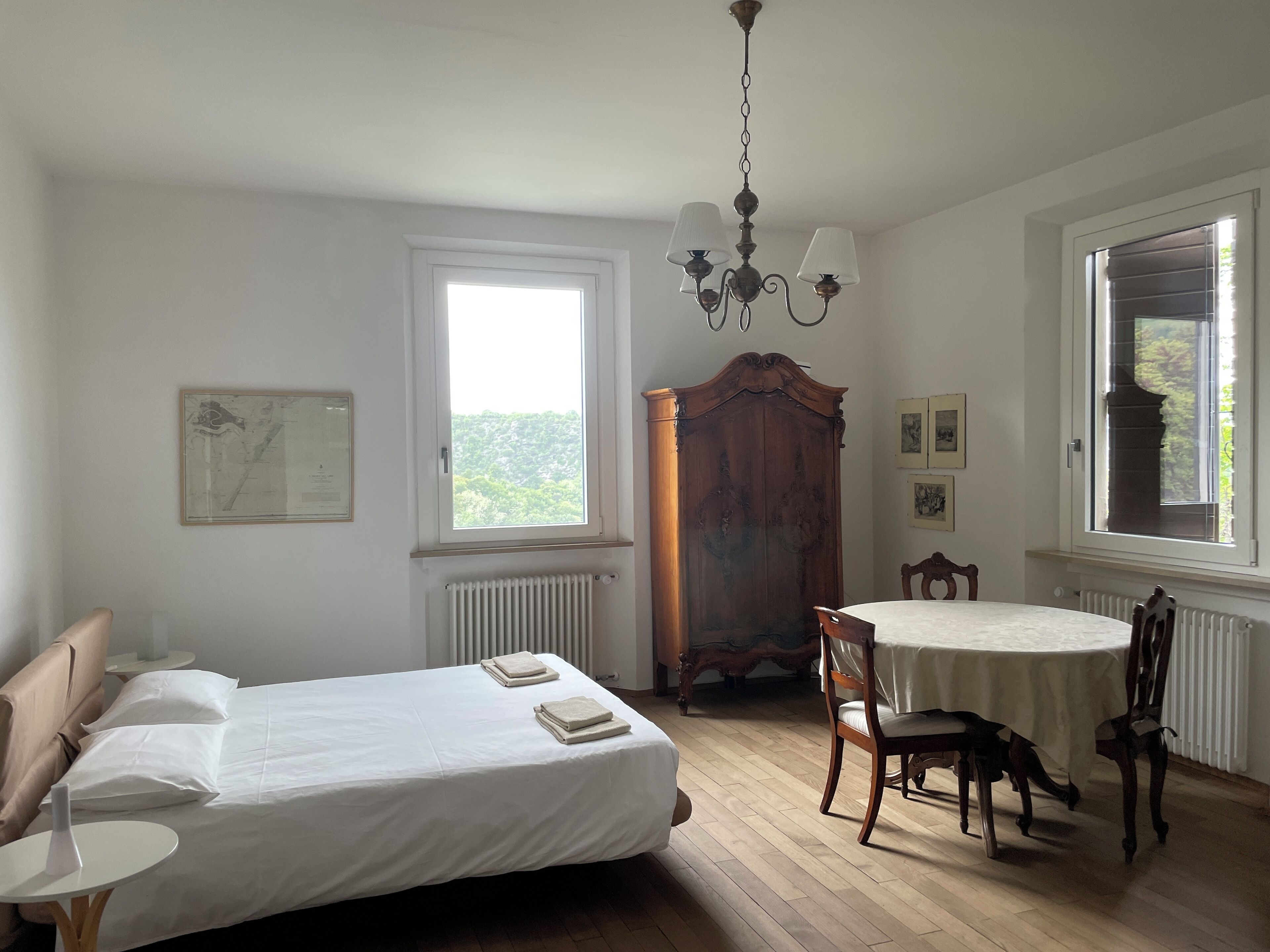 Ein Schlafzimmer mit einem Bett, einem runden Tisch mit Stühlen, einem Holzschrank und einem Fenster mit Jalousien.