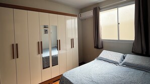 Un dormitorio con cama, armario y ventana con cortinas.
