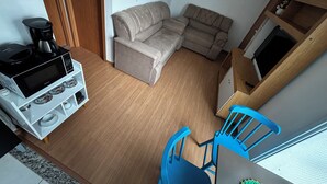 Un espacio habitable pequeño con sofá, cafetera, una silla azul y una estantería de madera.