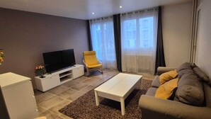 Un soggiorno moderno con una TV a schermo piatto, una poltrona gialla, un tavolino da caffè bianco e un divano grigio.