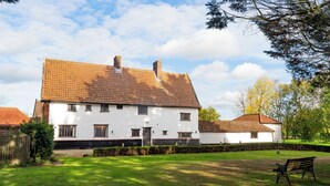 Une maison blanche avec un toit en tuiles, une porte d’entrée et un petit jardin devant, agrémenté d’un banc.