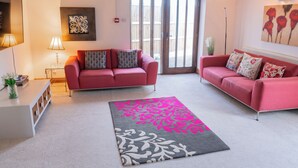 Un salon chaleureux avec deux canapés rouges, un tapis à motifs gris et rose, et un plafond en bois.