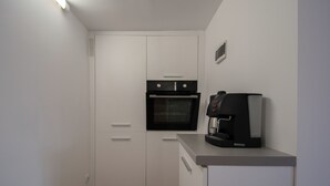 Eine kleine Küchenzeile mit eingebautem Backofen, einer Kaffeemaschine und weißen Schränken.