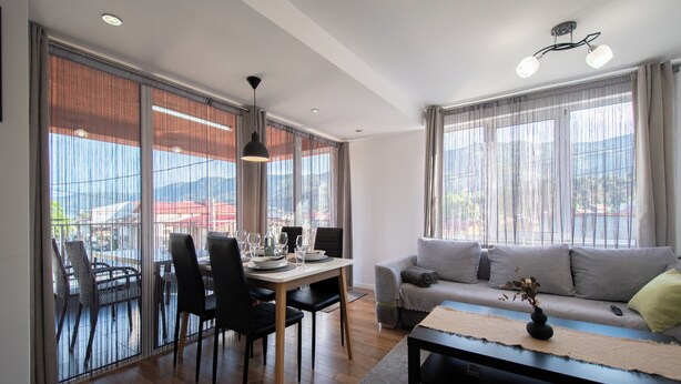 Ein modernes Wohnzimmer mit Essbereich, großen Fenstern und einer Couch.