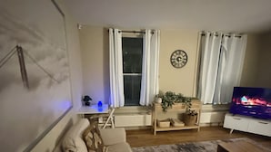 Ein Wohnzimmer mit einer Couch, einem Couchtisch, einem Fernseher und einem Fenster mit Vorhängen.