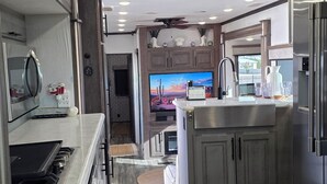 A modern RV kitchen with stainless steel appliances, a flat-screen TV, and a dining area with a patterned rug. - Luxury Glamping Oasis: Superstition Mtns, Views & Nearby Lakes (Apache Junction)