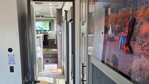 A narrow hallway with a television displaying a scenic view, wooden flooring, and a small rug. - Luxury Glamping Oasis: Superstition Mtns, Views & Nearby Lakes (Apache Junction)