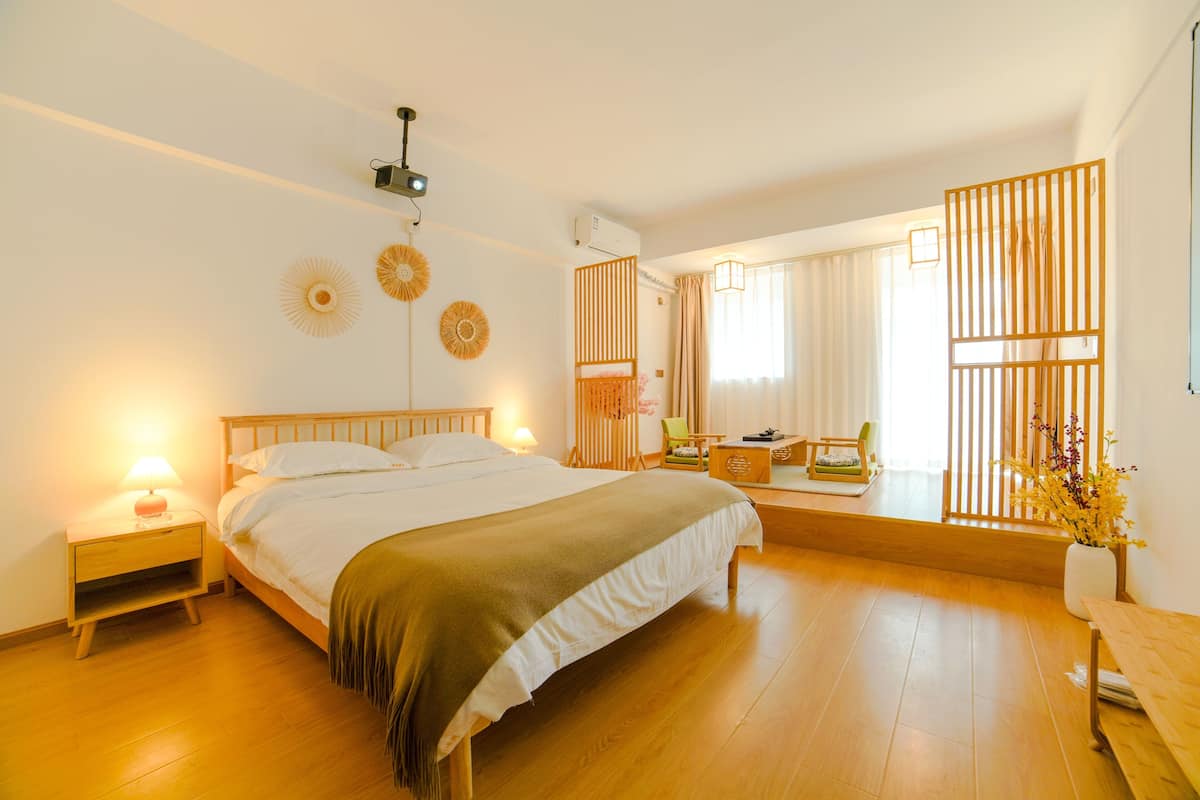 Ein helles Schlafzimmer mit einem großen Bett, Nachttischen, Holzboden und einem Fenster mit Vorhängen.