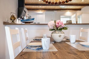 Una mesa de comedor con sillas blancas, un jarrón con flores y un techo de madera.