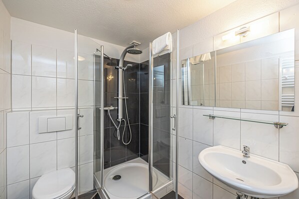 Un baño moderno con ducha acristalada, un lavabo blanco y un espejo.