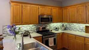 A kitchen with wooden cabinets, stainless steel appliances, a tiled backsplash, and a vase with flowers on the counter. - Comfort and calm in Ashland (Ashland)