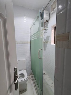 Une salle de bain compacte avec une douche à parois de verre, des toilettes et un sèche-mains.