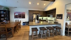 A spacious kitchen with a central island, wooden bar stools, and a dining area with a large table and chairs. - Snowcreek Resort Vacation Rental 1430 (Mammoth Lakes)