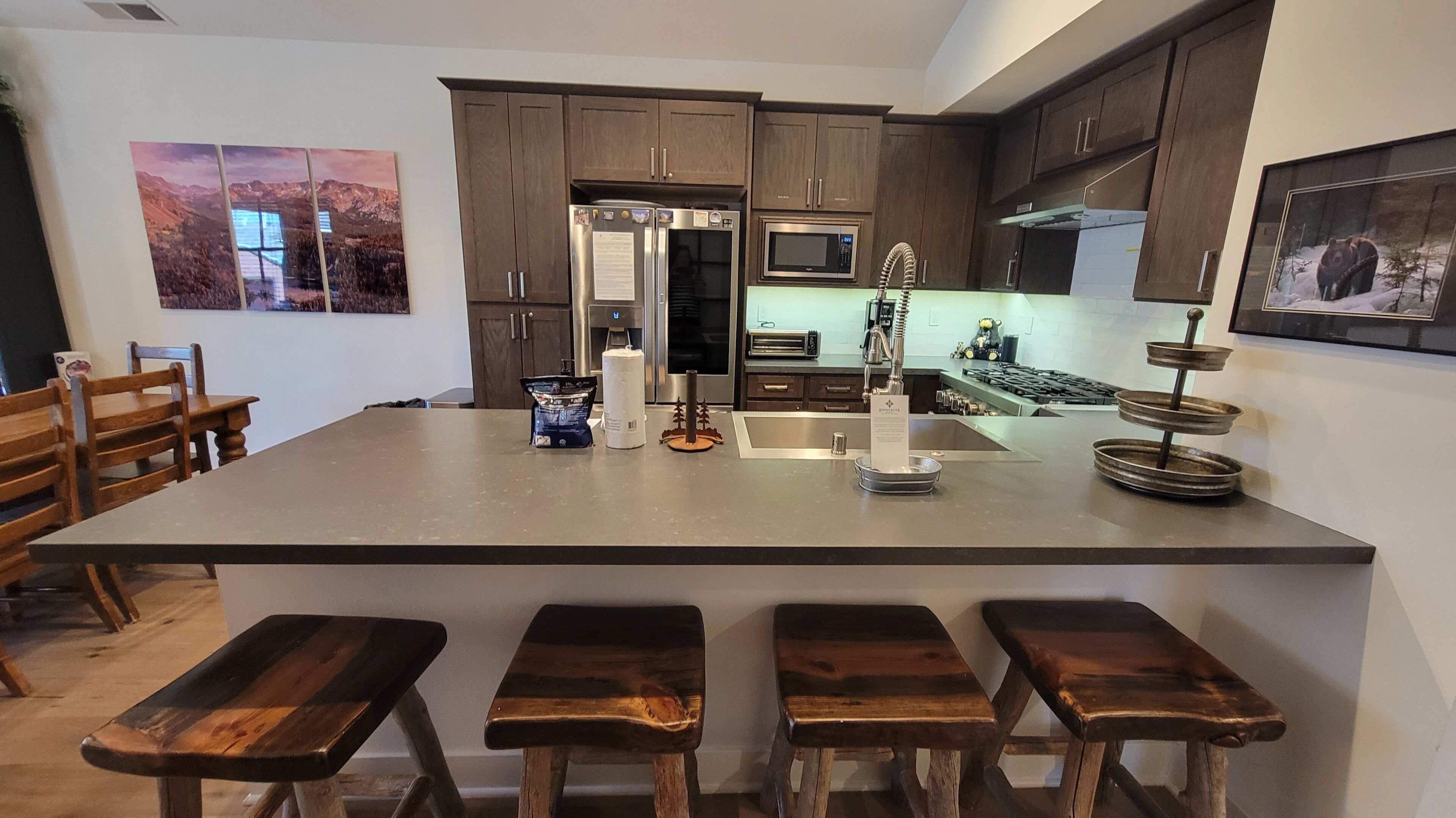 A kitchen with a central island, wooden bar stools, stainless steel appliances, and artwork on the walls.