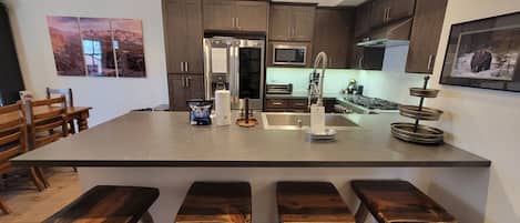 A kitchen with a central island, wooden bar stools, stainless steel appliances, and artwork on the walls.