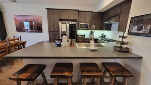 A kitchen with a central island, wooden bar stools, stainless steel appliances, and artwork on the walls.