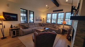 A living room with a sectional sofa, a coffee table, and a fireplace. There are large windows with blinds, a lamp, and a framed picture on the wall. - Snowcreek Resort Vacation Rental 1430 (Mammoth Lakes)
