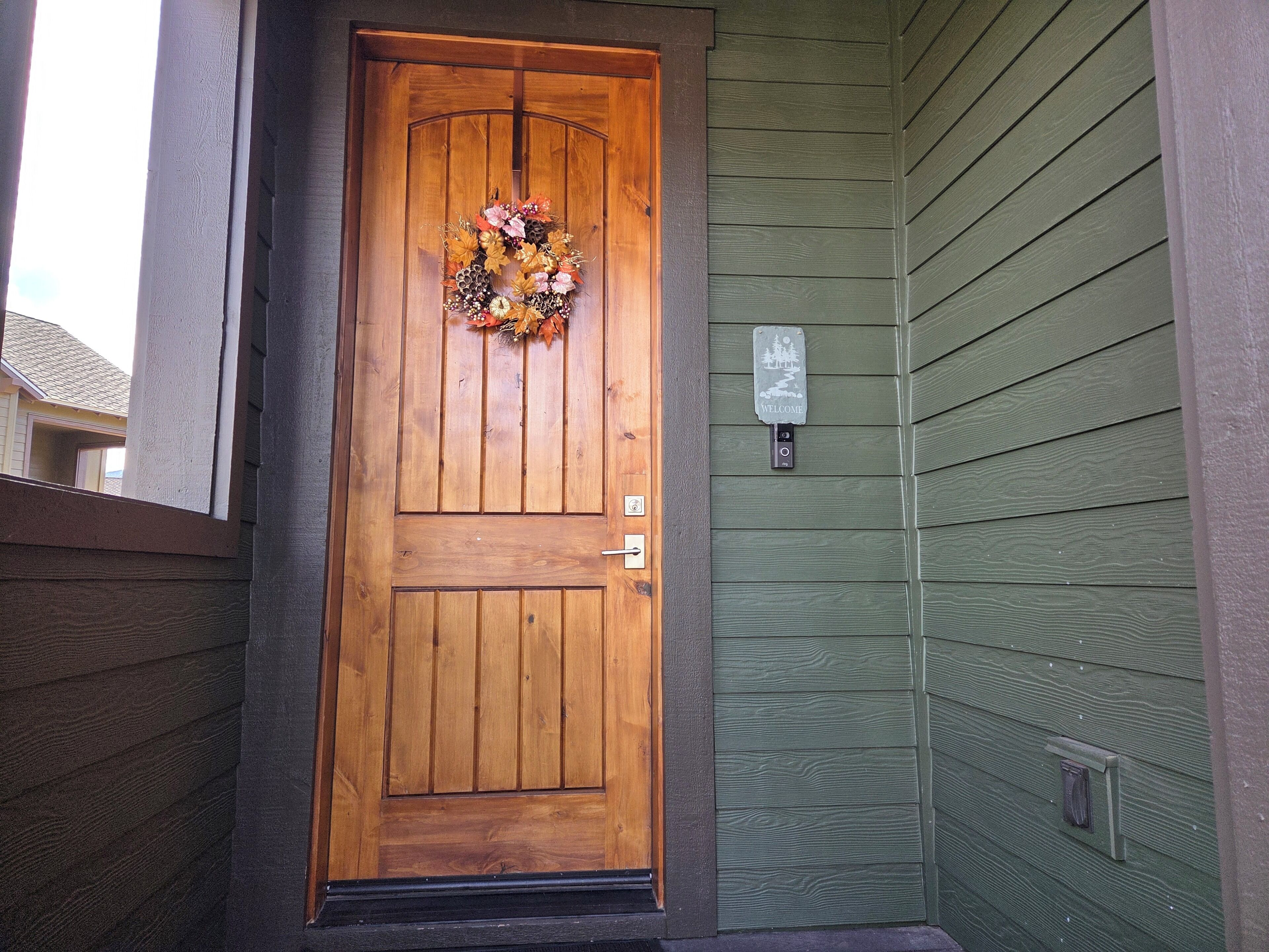 A wooden front door with a decorative wreath, a welcome sign, and a mailbox.