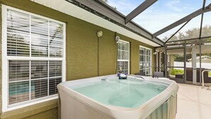 Un bain à remous situé dans un espace extérieur abrité, doté de grandes fenêtres et offrant une vue sur le paysage environnant.