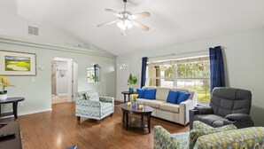 Un salon spacieux doté d’un plancher en bois franc, d’un ventilateur de plafond, d’un canapé, de fauteuils et d’une table basse.