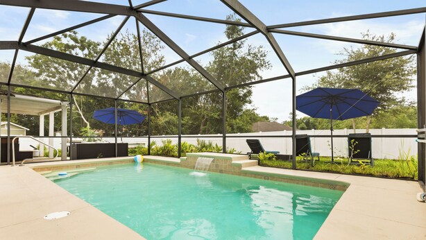 Une piscine couverte avec deux parasols, une chaise longue et une petite cascade décorative.