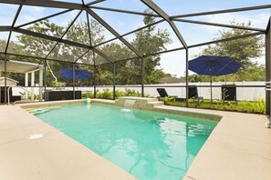 Une piscine couverte avec deux parasols, une chaise longue et une petite cascade décorative.