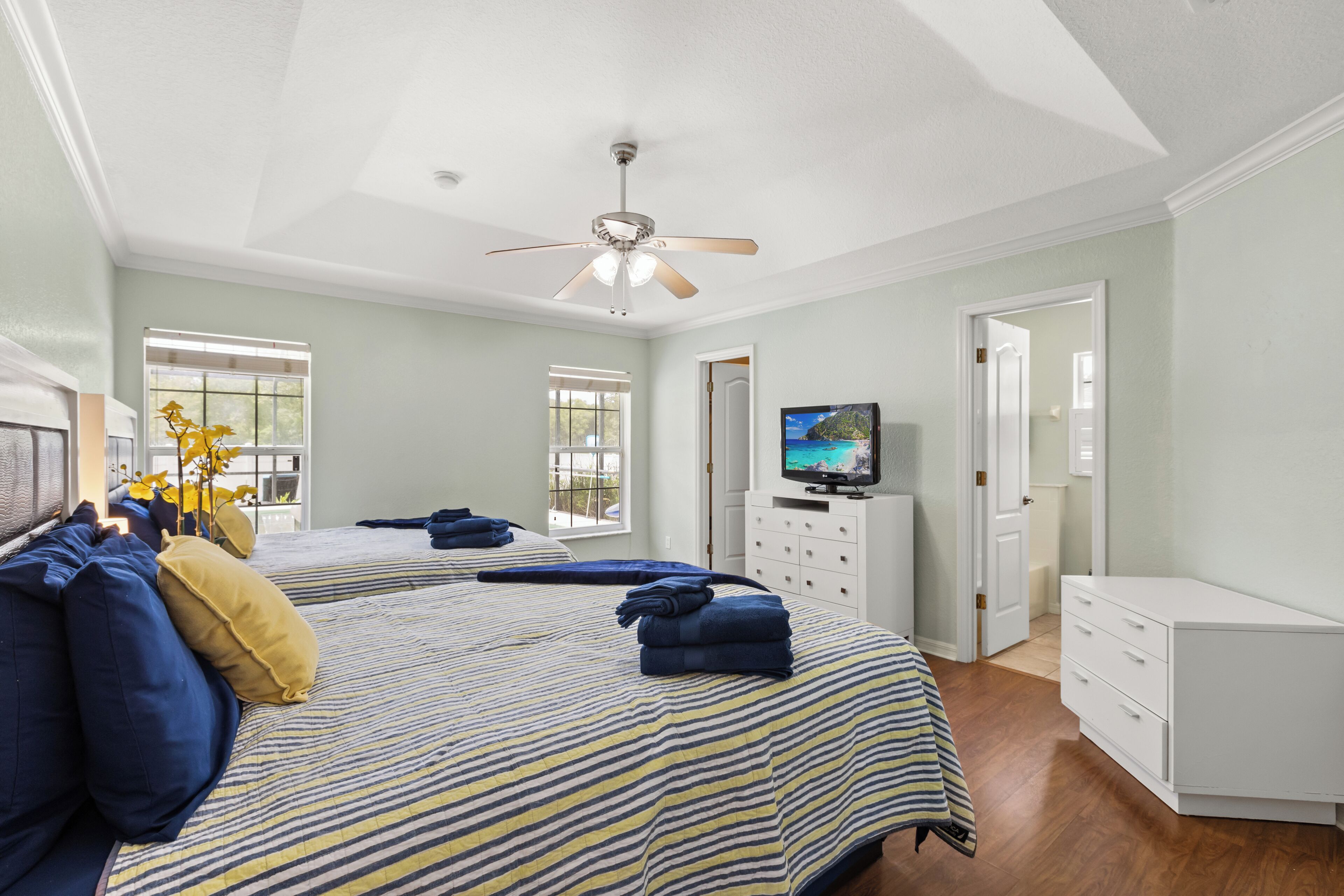 A bedroom with two beds, a ceiling fan, a TV, and a dresser.