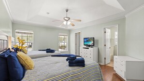 Une chambre avec deux lits, un ventilateur de plafond, une télévision et une commode.