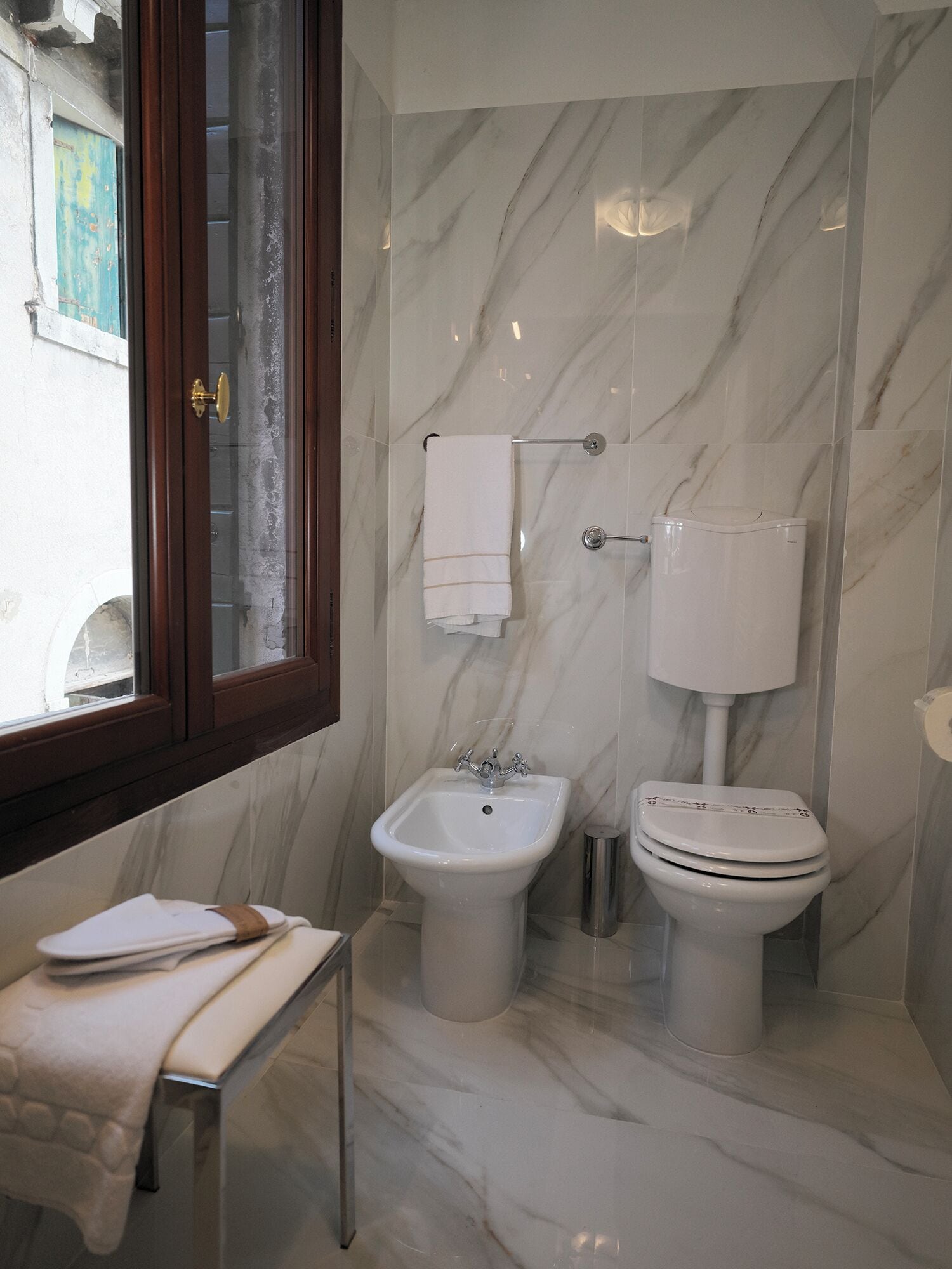 A bathroom with a bidet, toilet, and a window with a view of the outside.