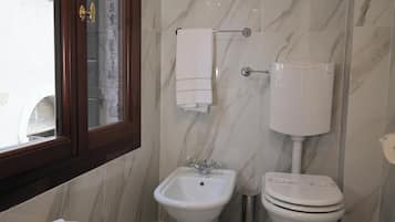 A bathroom with a bidet, toilet, and a window with a view of the outside.