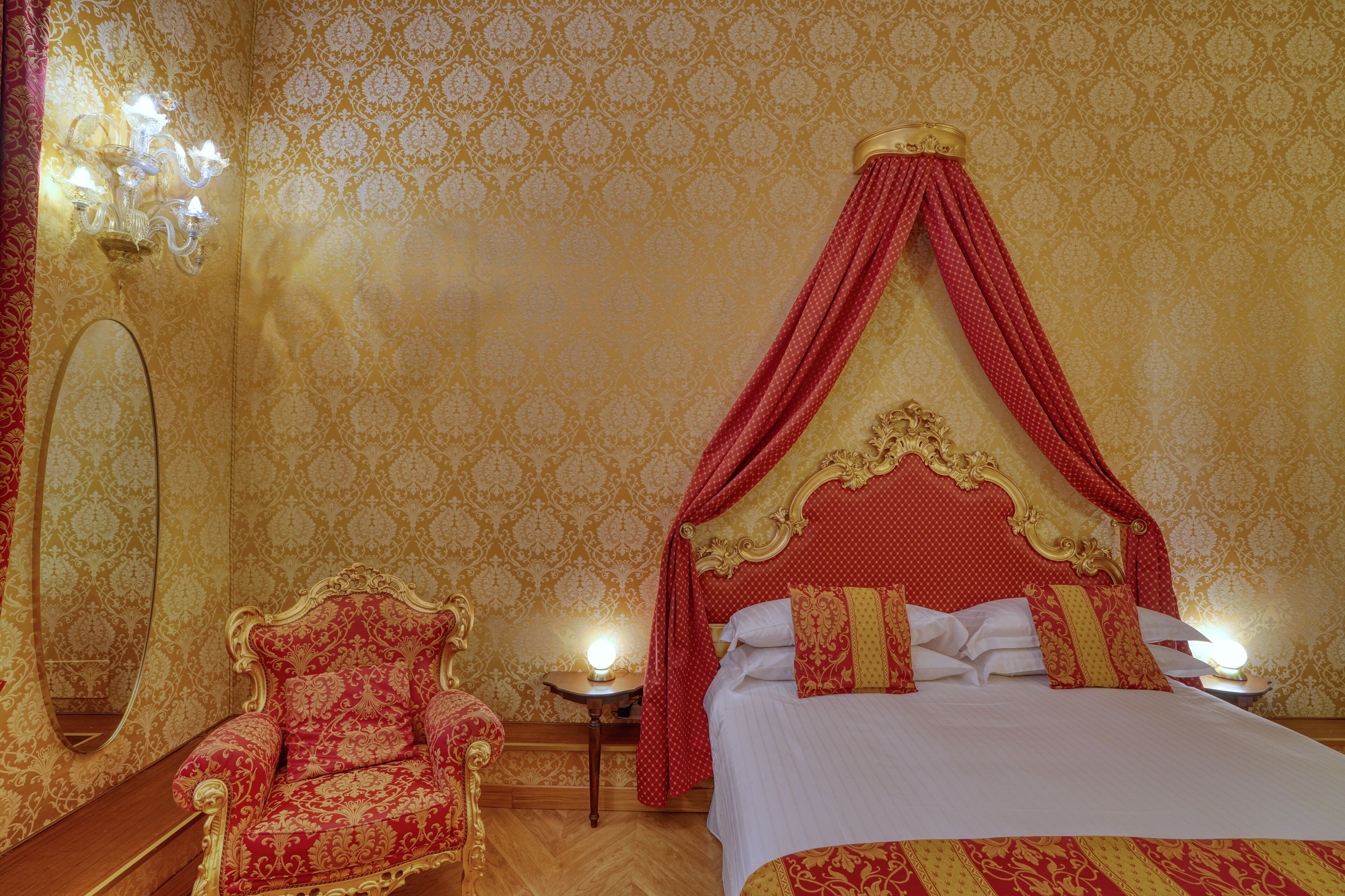 A luxurious bedroom with a canopy bed, ornate chair, and a mirror.