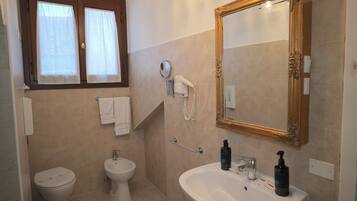 Une salle de bain équipée de toilettes, d’un bidet, d’un lavabo, d’un miroir et d’un sèche-cheveux fixé au mur.