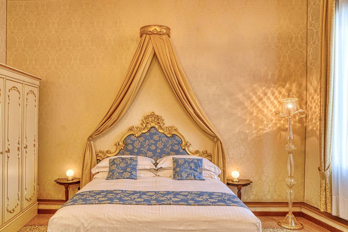 A bed with a canopy, a nightstand with a lamp, and a tall floor lamp.