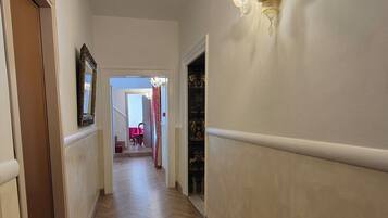 A hallway with a wooden herringbone floor, a wall-mounted light fixture, and a door on the left.