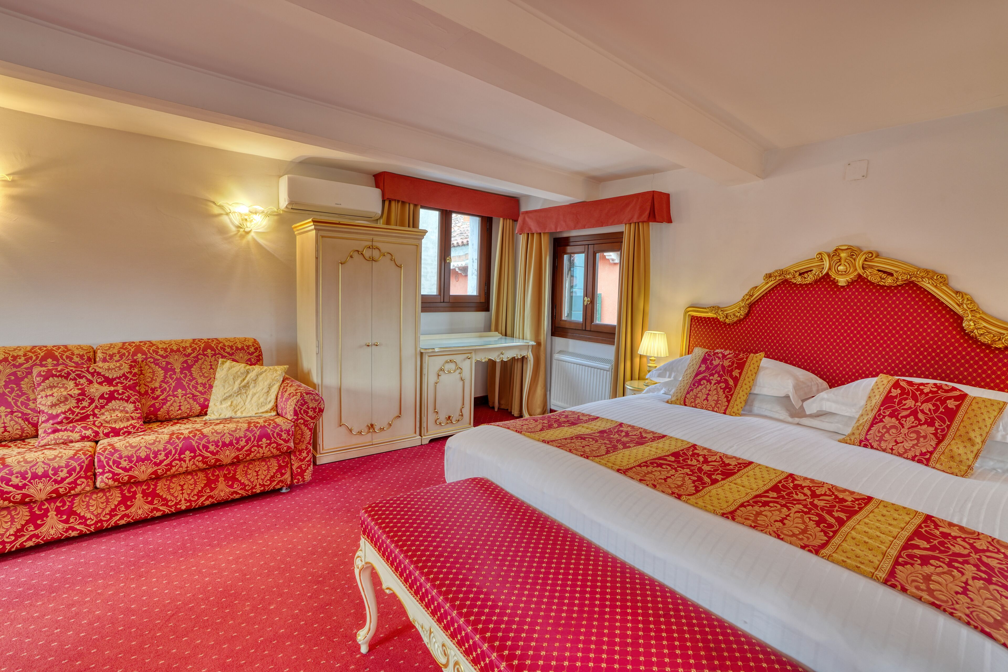 A hotel room with a large bed, a sofa, a desk, and a wardrobe.