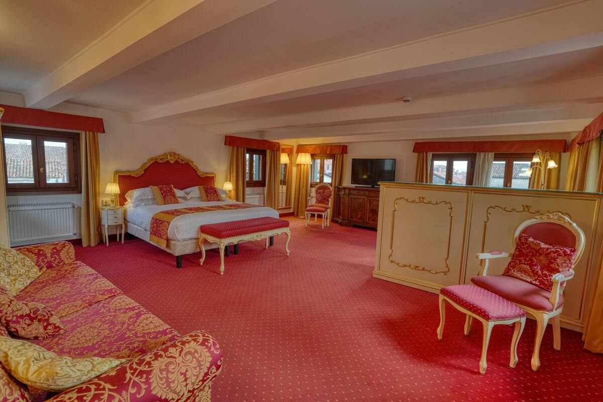 A hotel room with a large bed, a sofa, a chair, a TV, and a wardrobe.