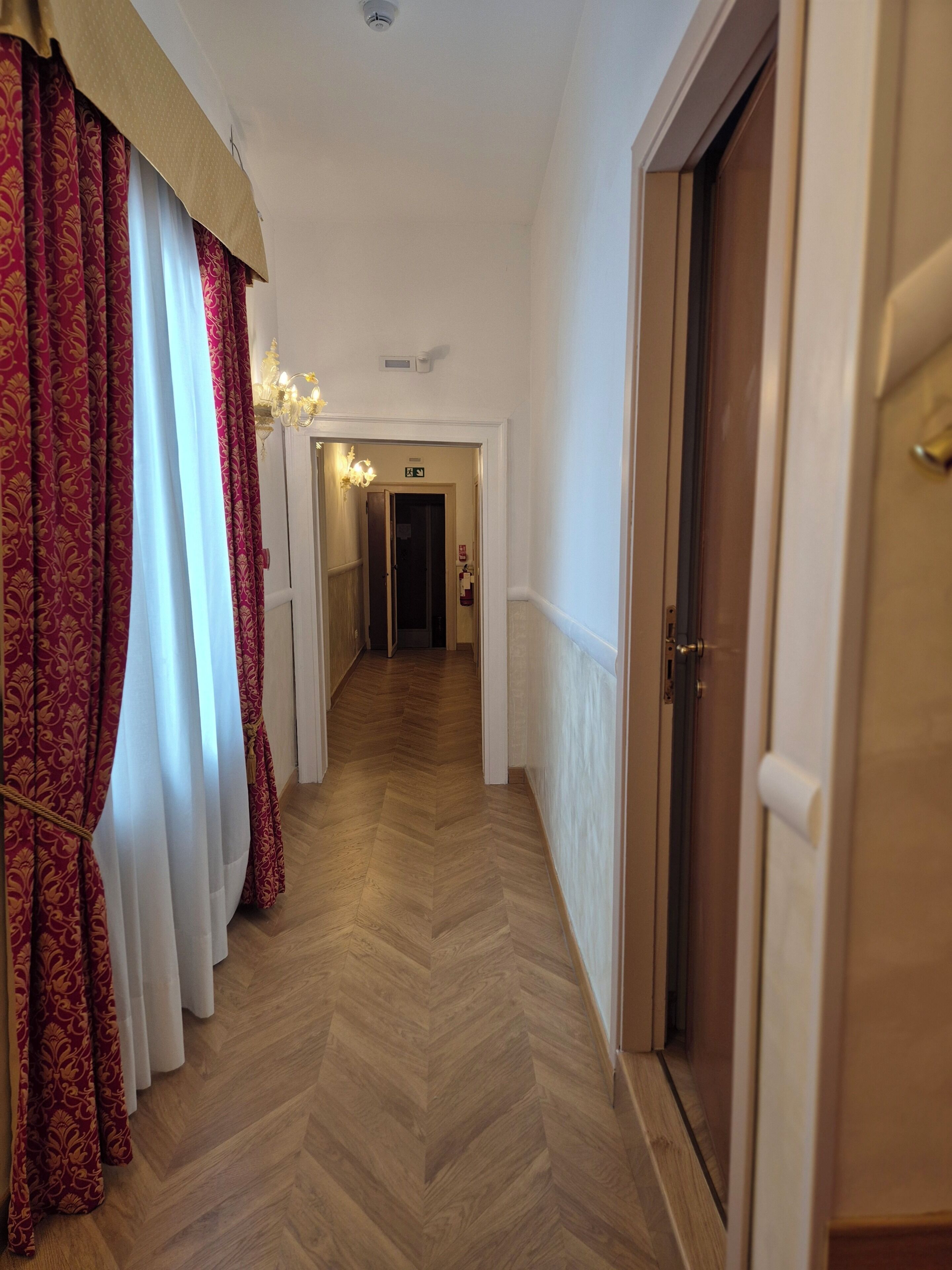 Un pasillo con cortinas estampadas, suelo de madera en espiga y una puerta a la derecha.