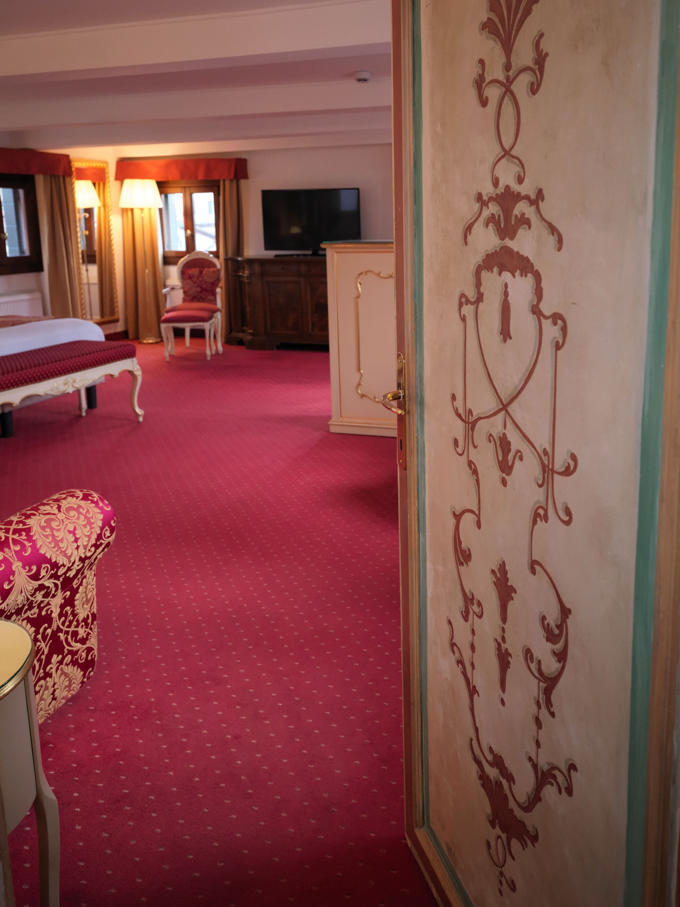 Quarto de hotel com cama, escrivaninha, televisão e armário.