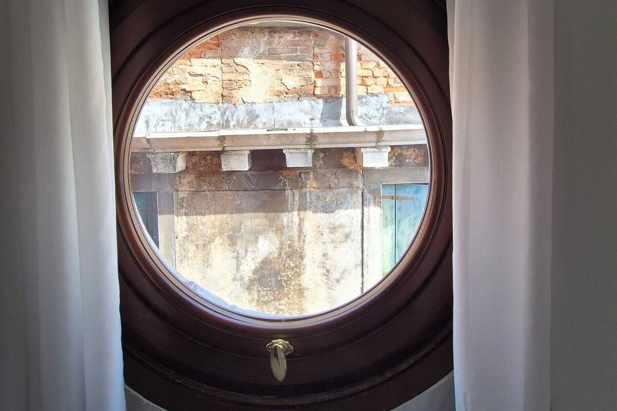 A round window with a wooden frame, curtains, and a view of a stone bridge.