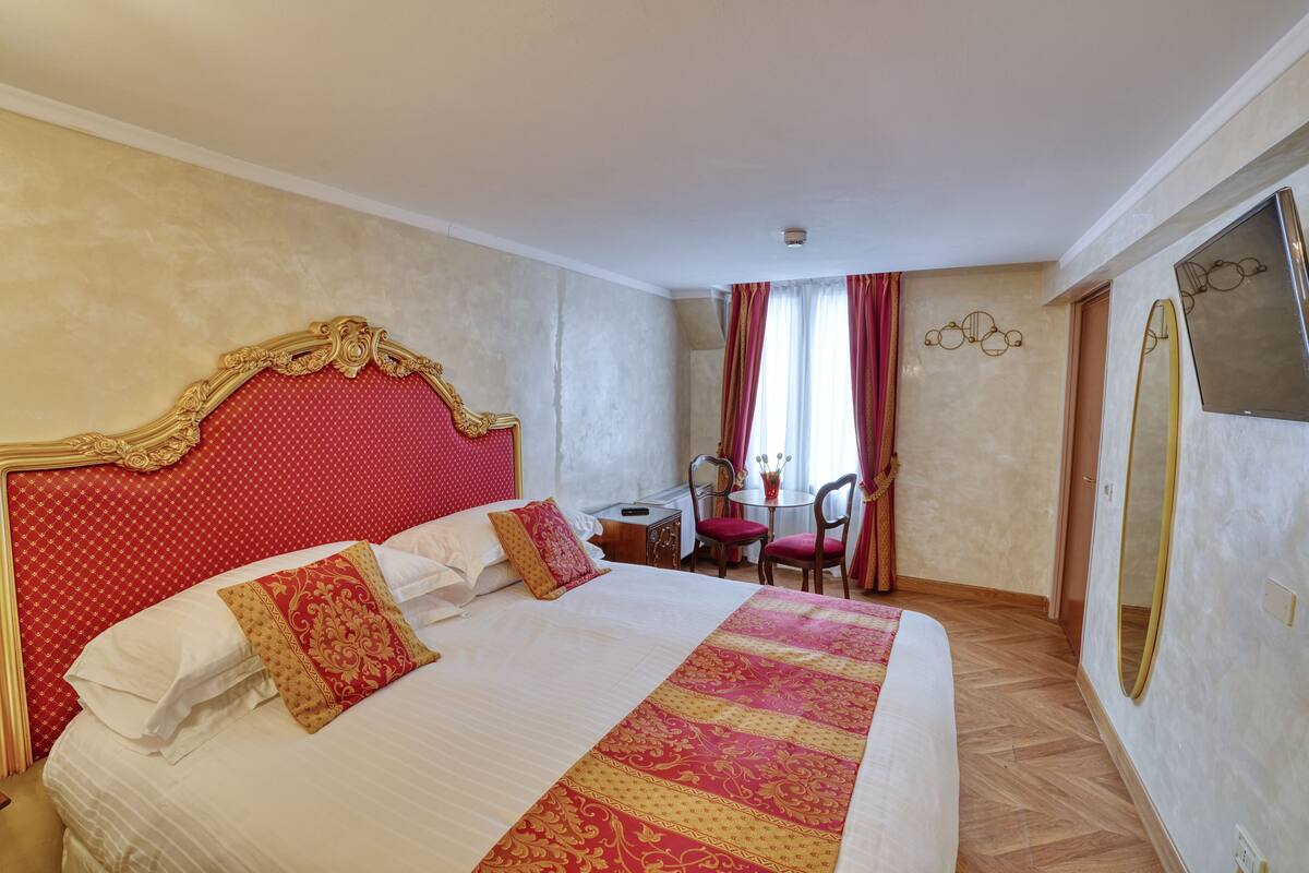 A hotel room with a large bed, a desk, a chair, and a mirror.