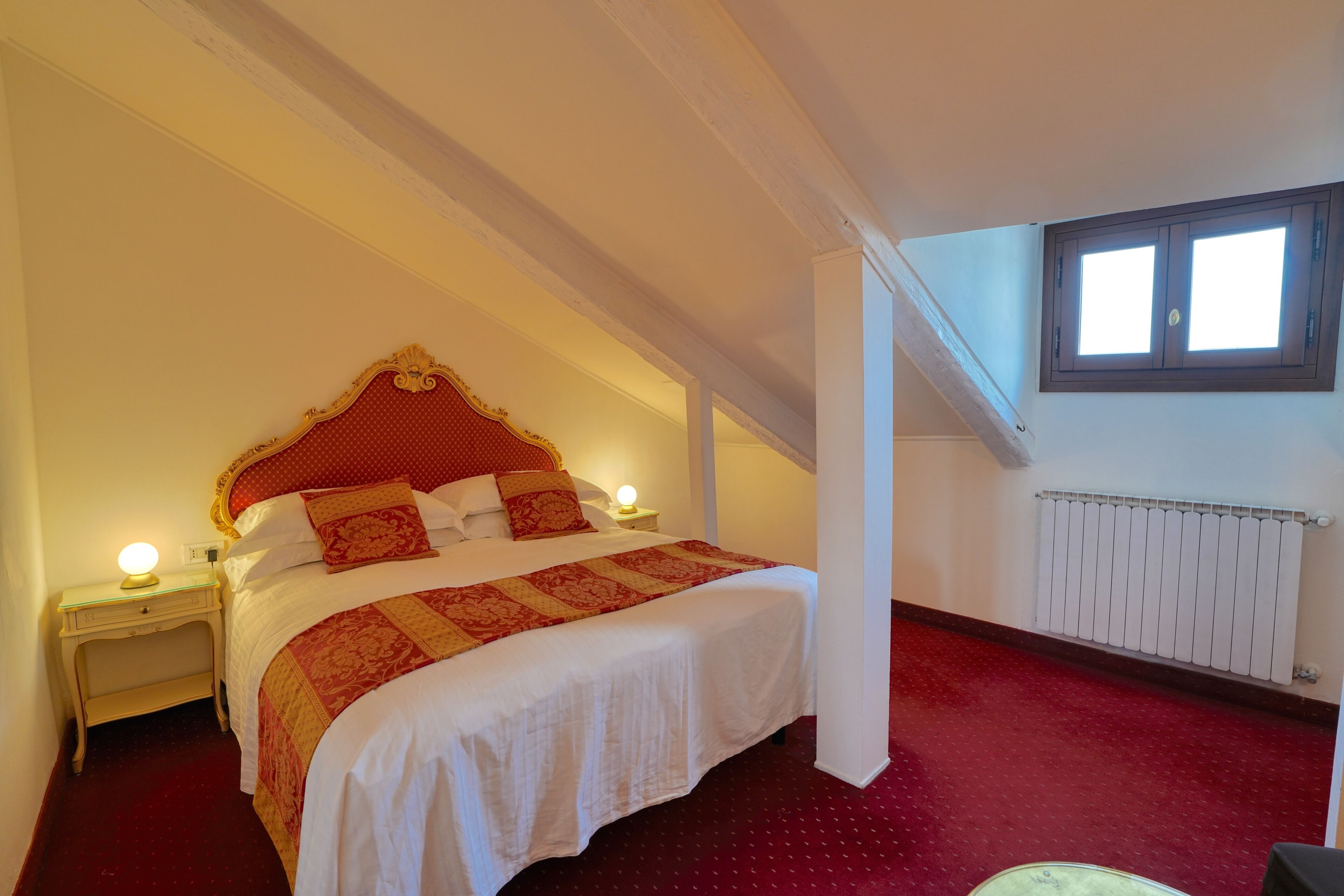 Ein Schlafzimmer mit einem großen Bett, einem Nachttisch mit Lampe, einem Fenster und einer Heizung.