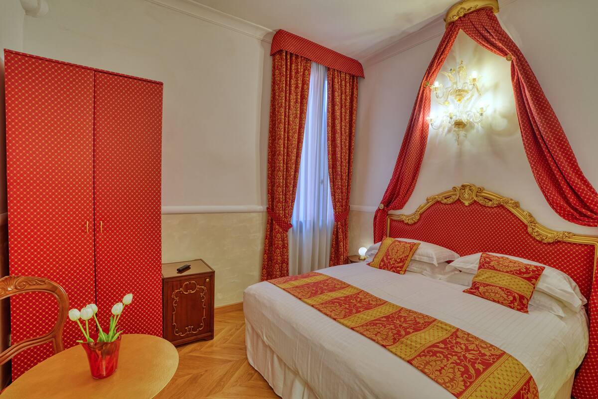 A hotel room with a bed, a chair, a table, and a vase of flowers.