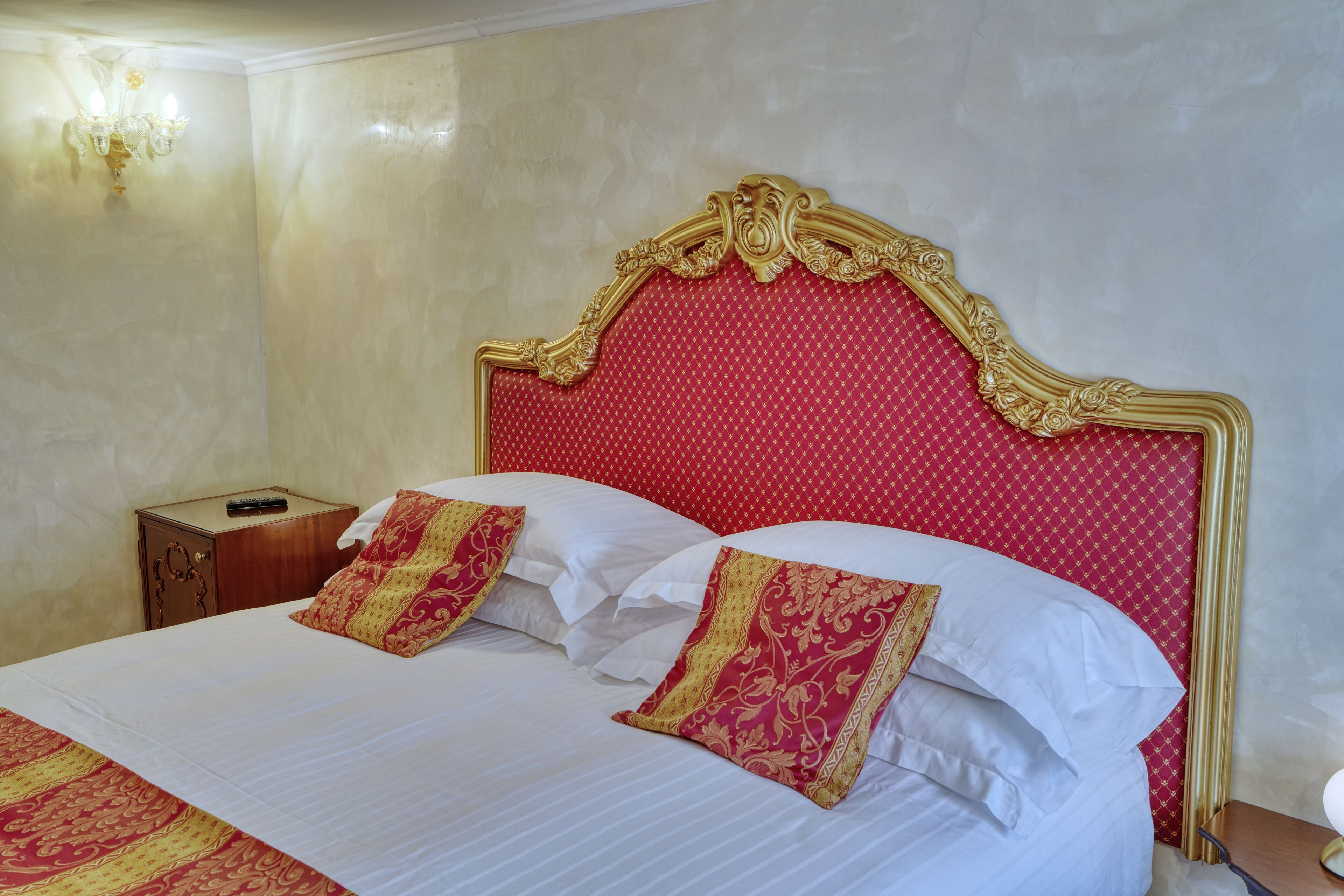 A hotel room with a large bed, a wooden nightstand, and a wall-mounted light fixture.