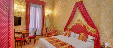 A room with a four-poster bed, a round wooden table with chairs, a television, and a chandelier.