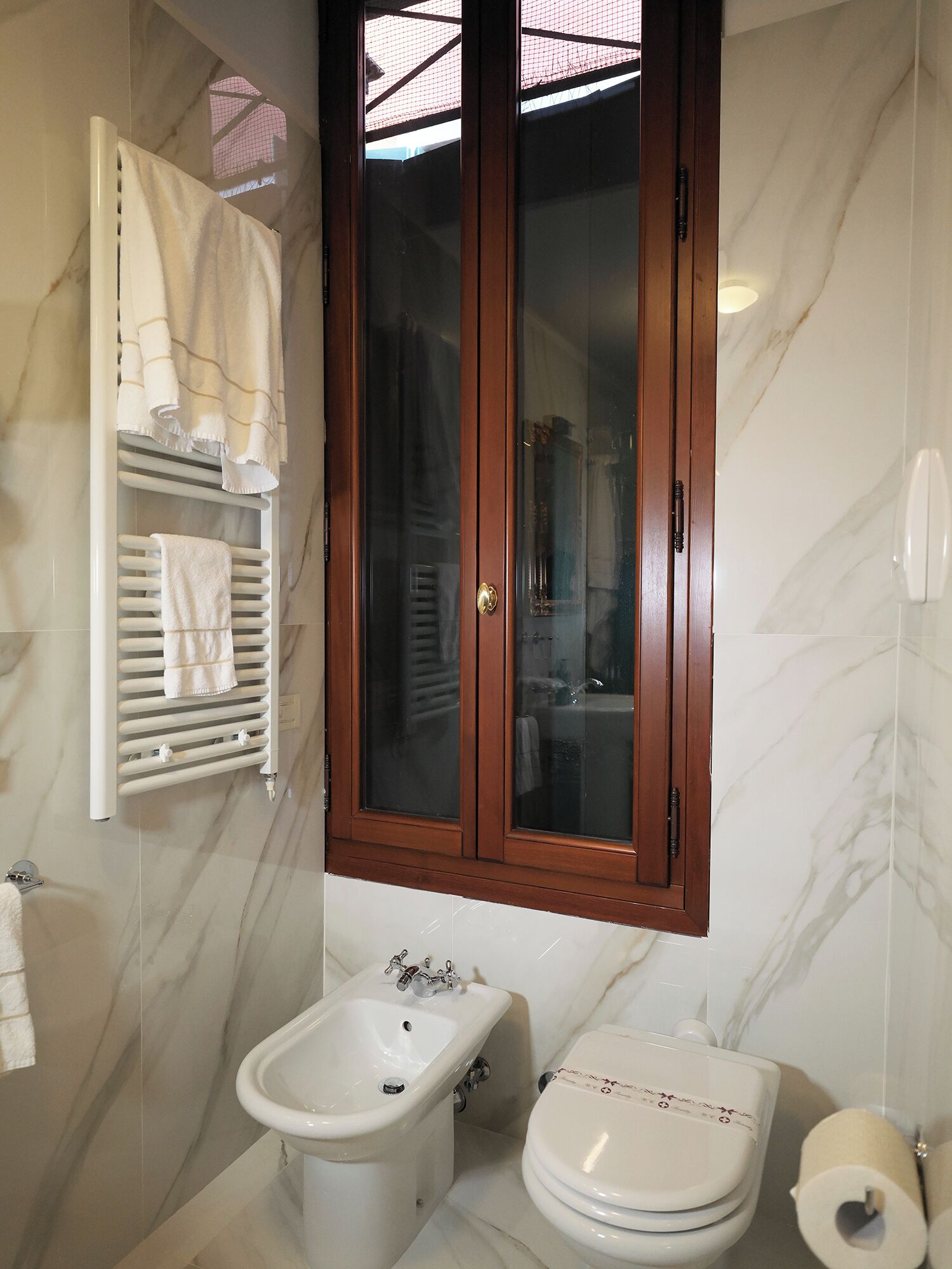 A bathroom with a marble wall, a wooden medicine cabinet, a bidet, and a toilet.
